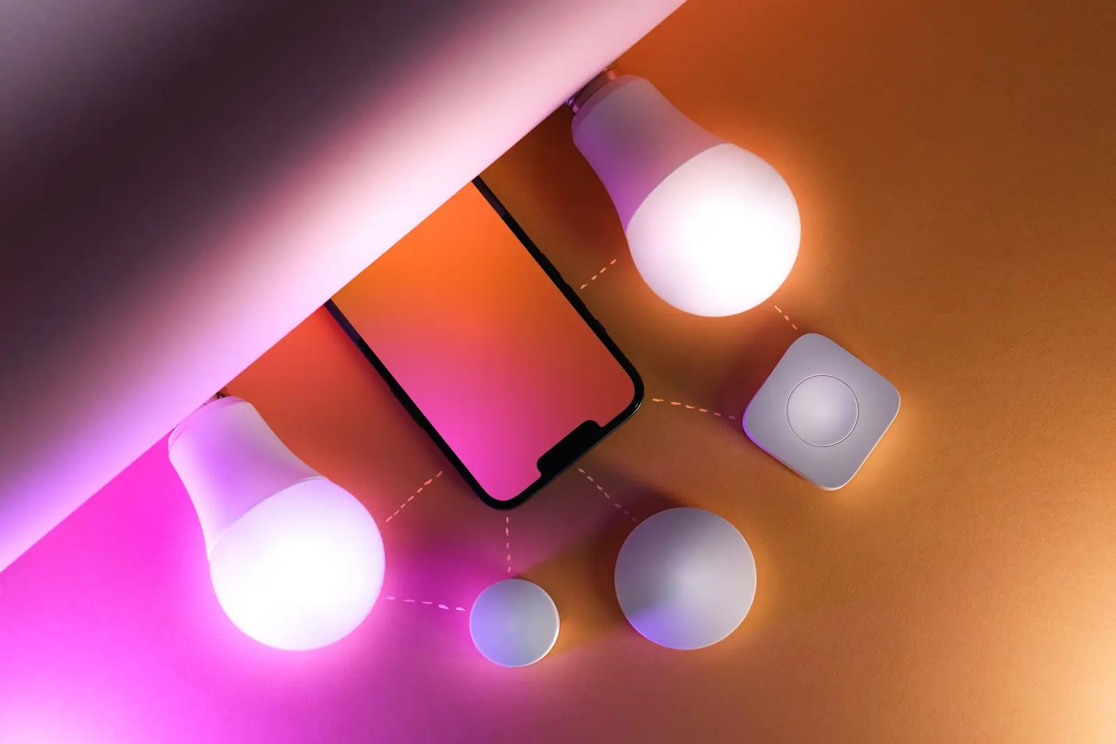 Smart LED light bulbs glowing pink next to a smartphone