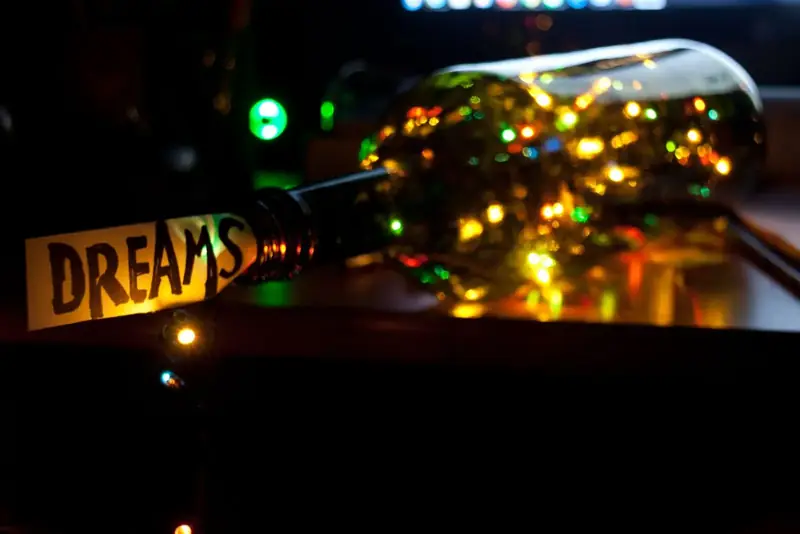 Glass bottle filled with fairy lights and a rolled dreams note tucked in its neck