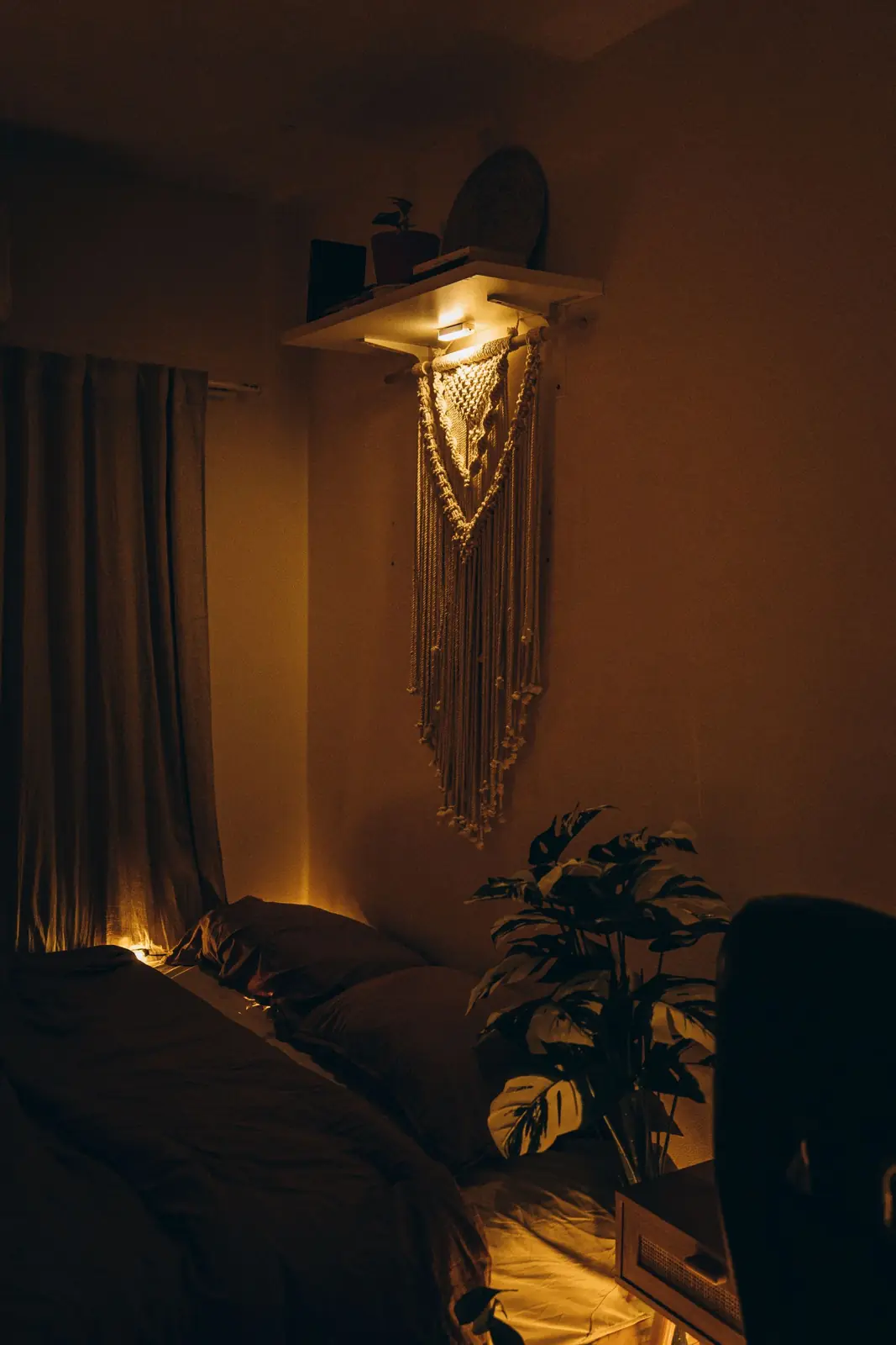 Cozy bedroom lit by warm lamp light with macrame on the wall